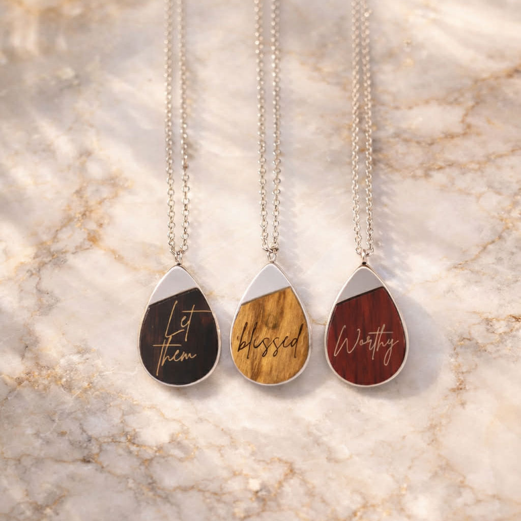 Three teardrop-shaped necklaces with engraved text on a marble surface