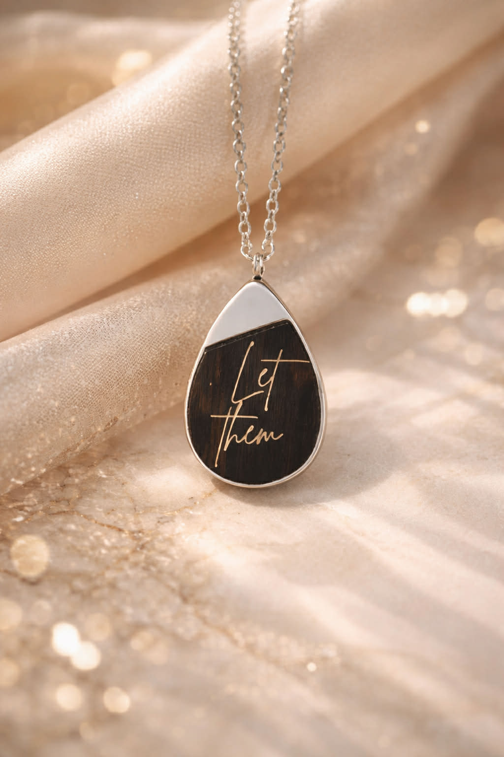 Teardrop-shaped African Blackwood pendant with 'Let Them' laser engraving on a beige fabric background