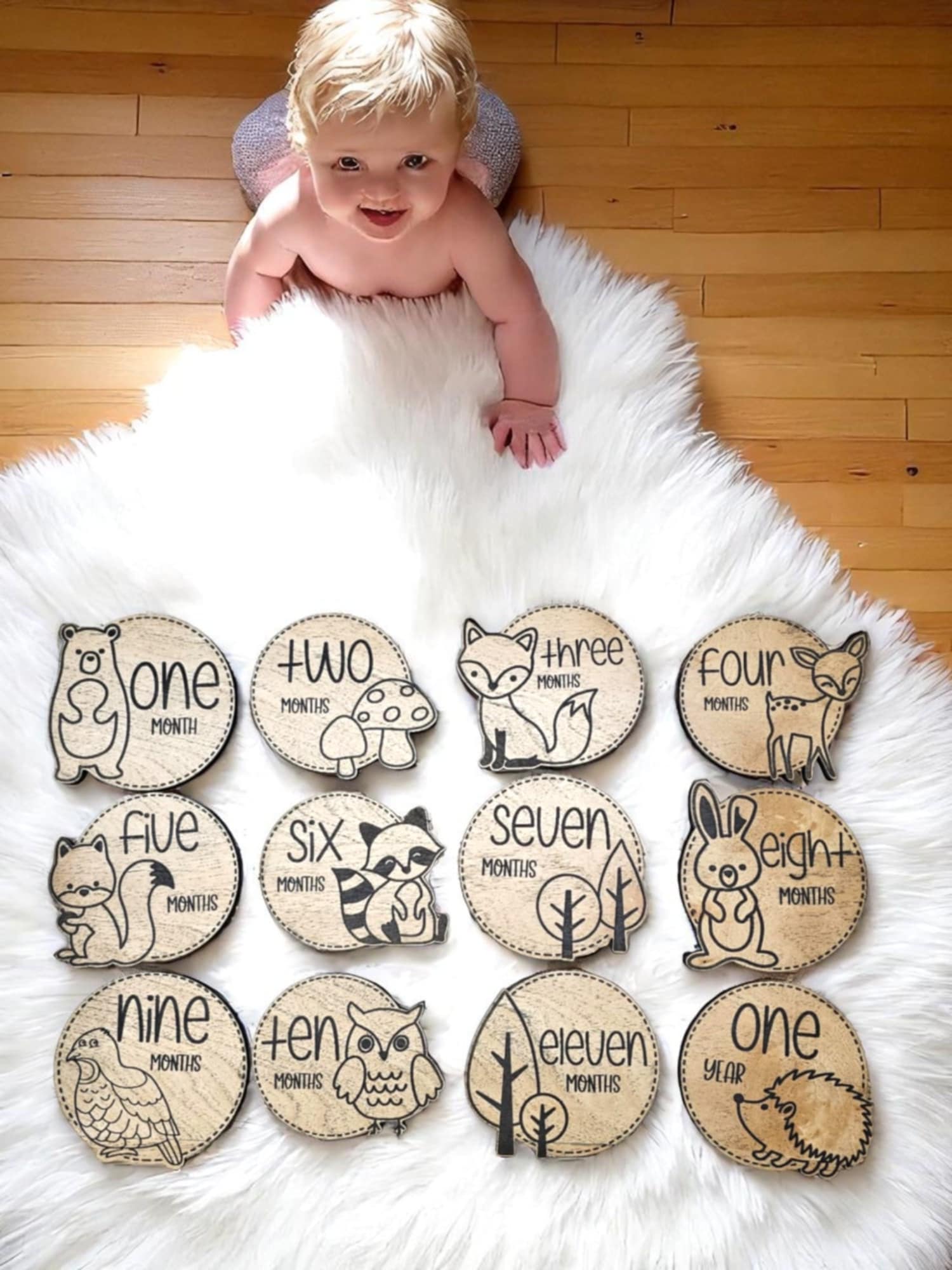 Laser engraved wooden baby photo milestone markers featuring baby woodland animals on each one laying on a white fur rug with a baby in background
