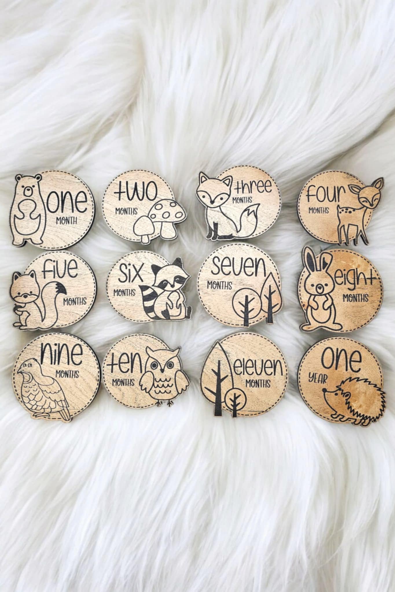 Laser engraved wooden baby photo milestone markers featuring baby woodland animals laying on a white fur rug. 