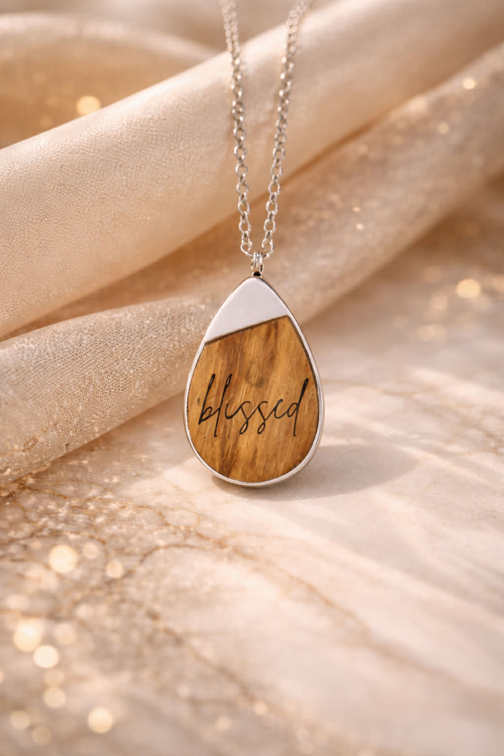 Teardrop-shaped necklace with Ironwood  pendant and laser engraved with 'blessed' on a soft fabric background
