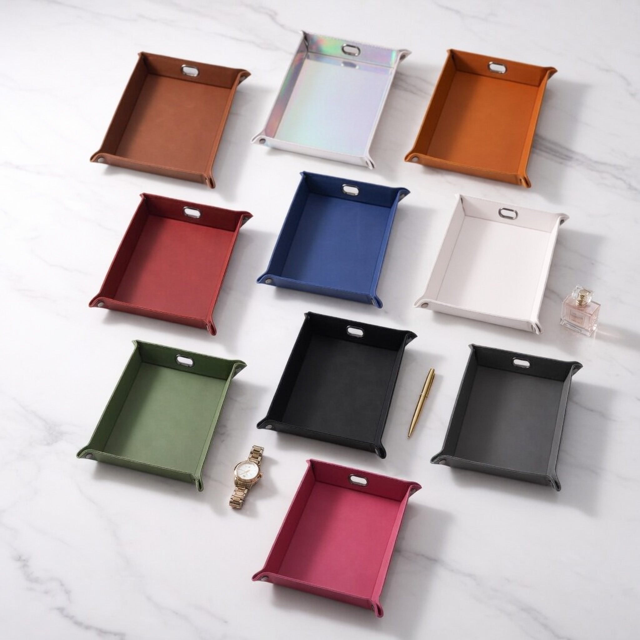 Ten rectangular Laserette storage trays in assorted colors are arranged on a white marble surface. The trays include brown, iridescent, rawhide, red, blue, white, green, black, gray, and pink.