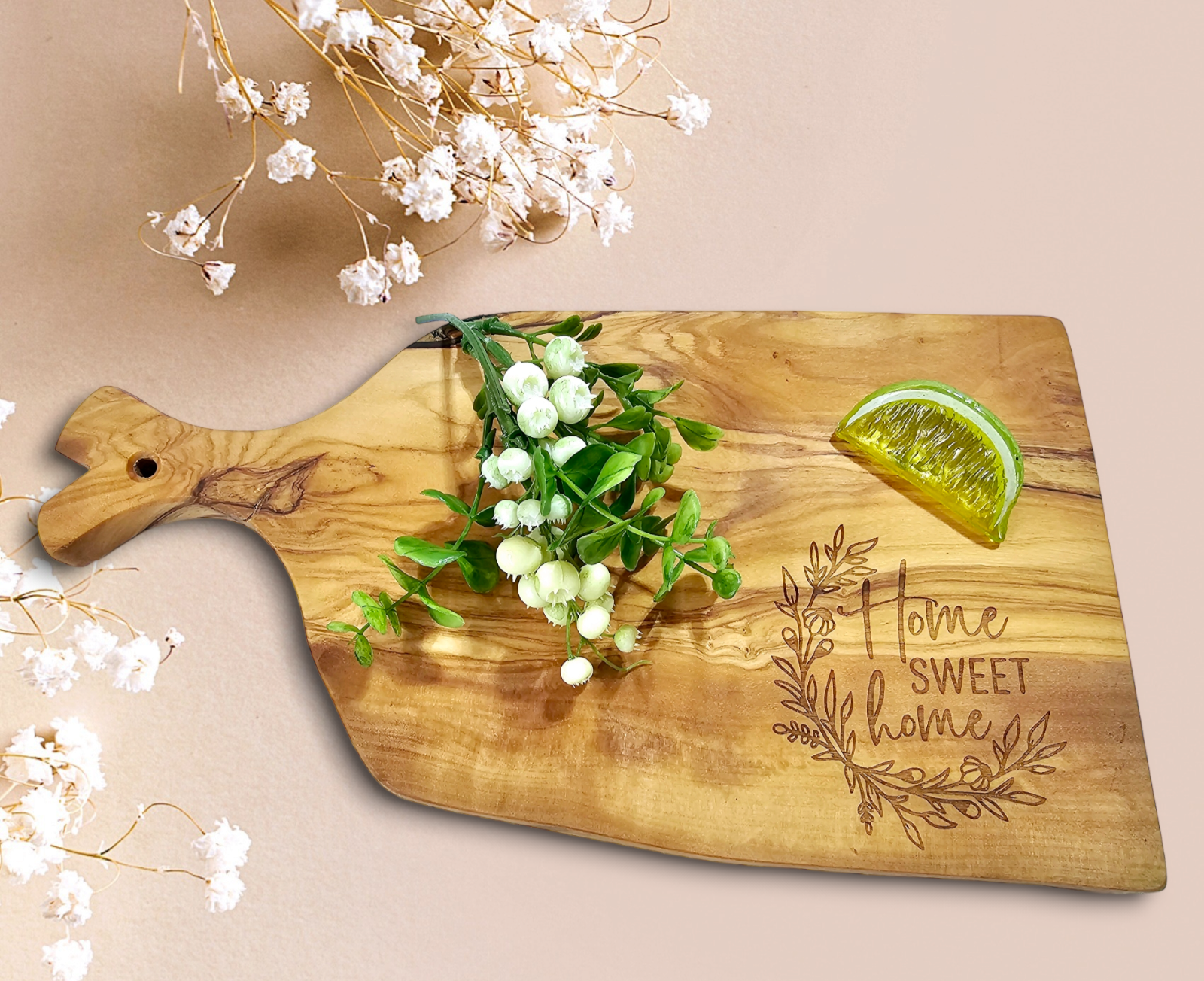 An olivewood cutting board with a personalized engraving, displayed with a white flower and a slice of lemon, against a beige background.