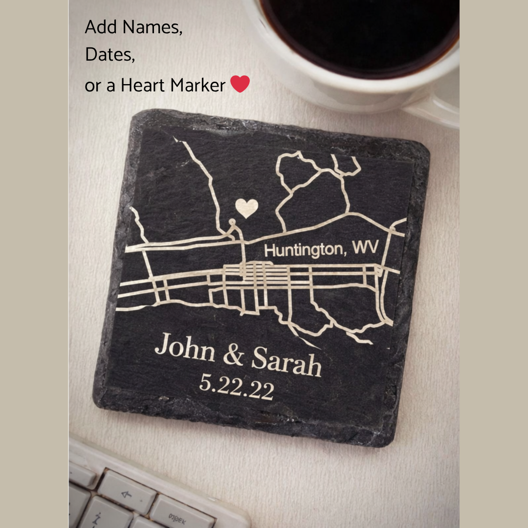 Personalized slate coaster with map design, names, and date on a surface with a cup of coffee.
