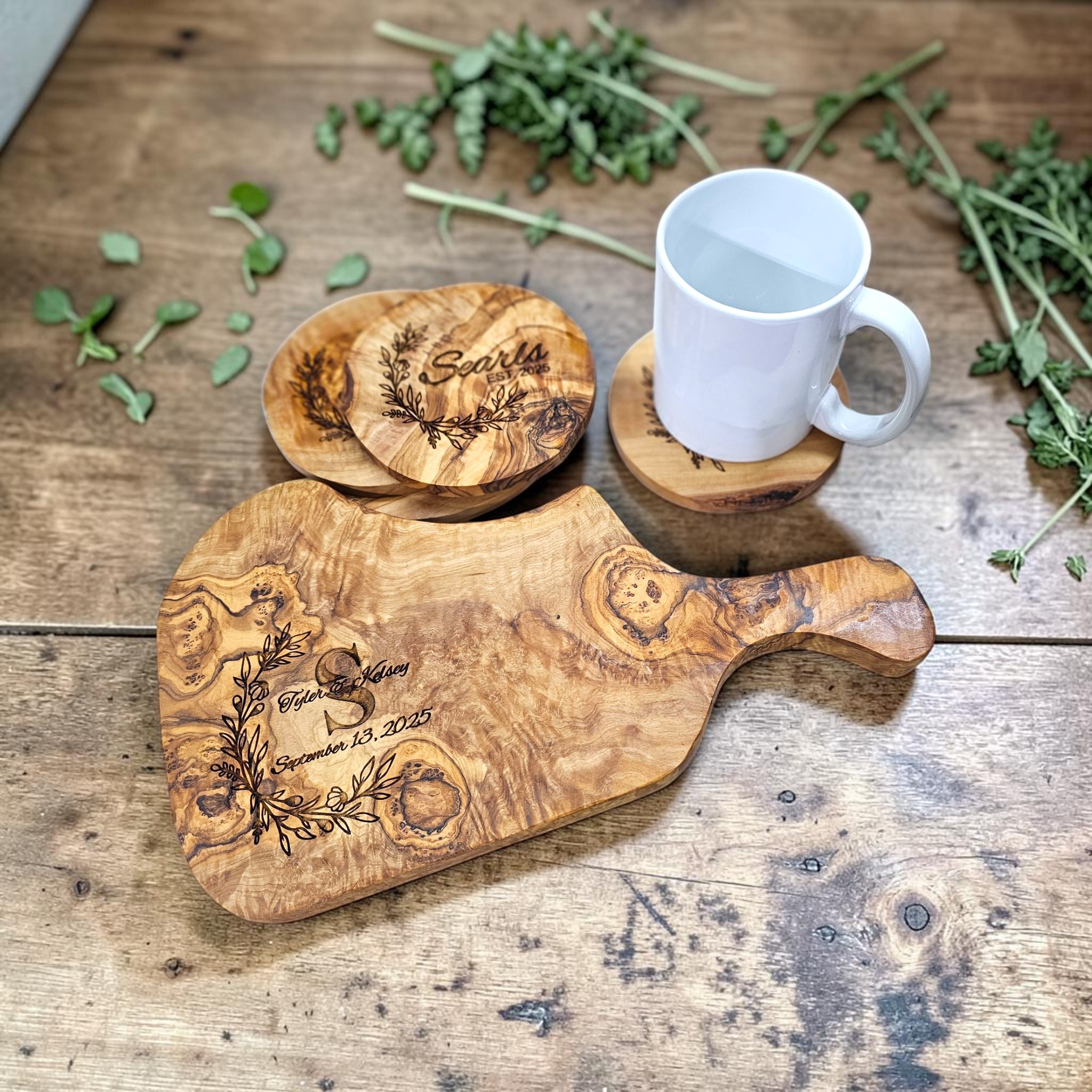 Engraved board and coasters on wooden background with herbs and a coffee mug